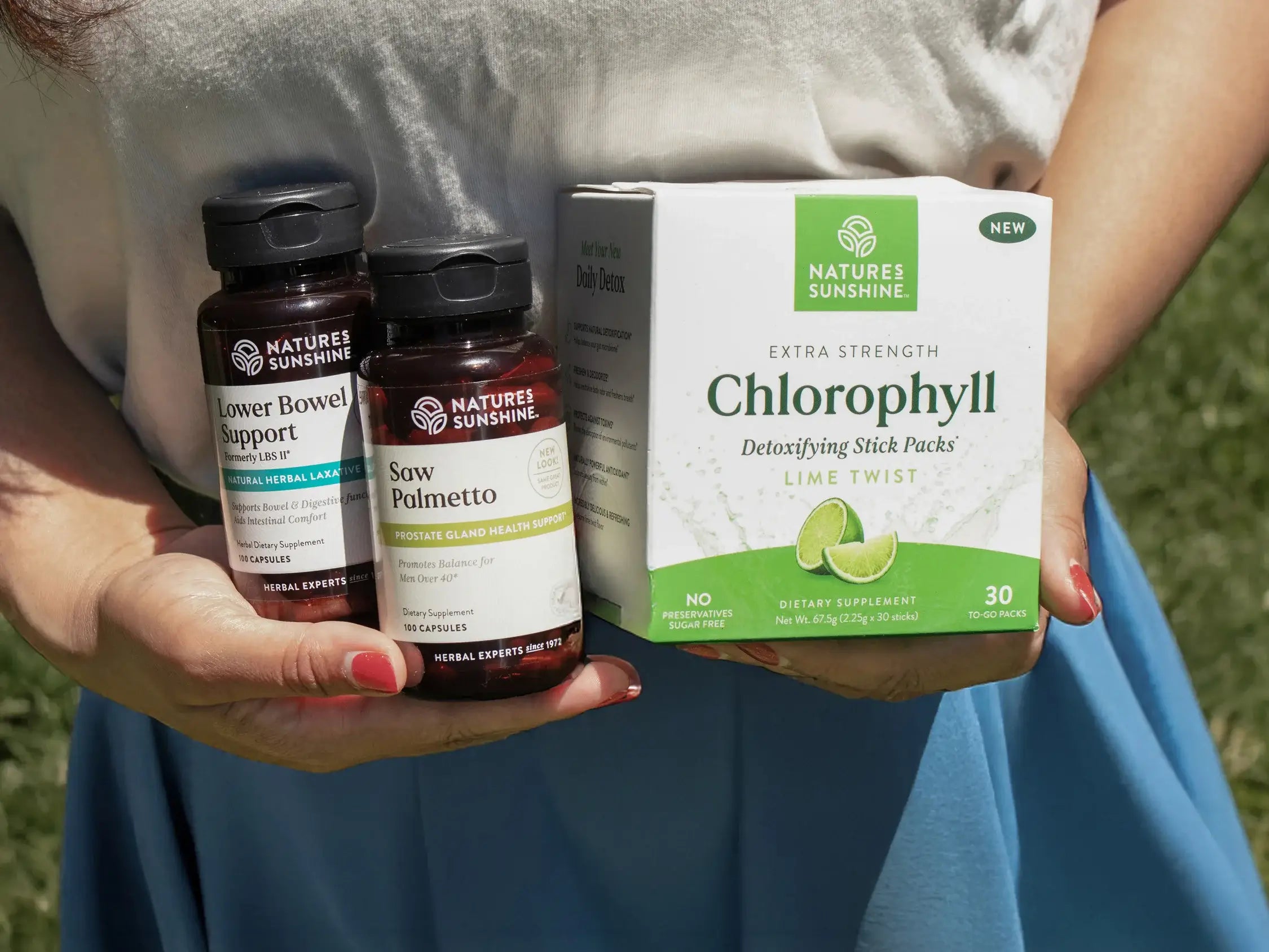 Person holding Nature's Sunshine supplement products against a grassy background.
