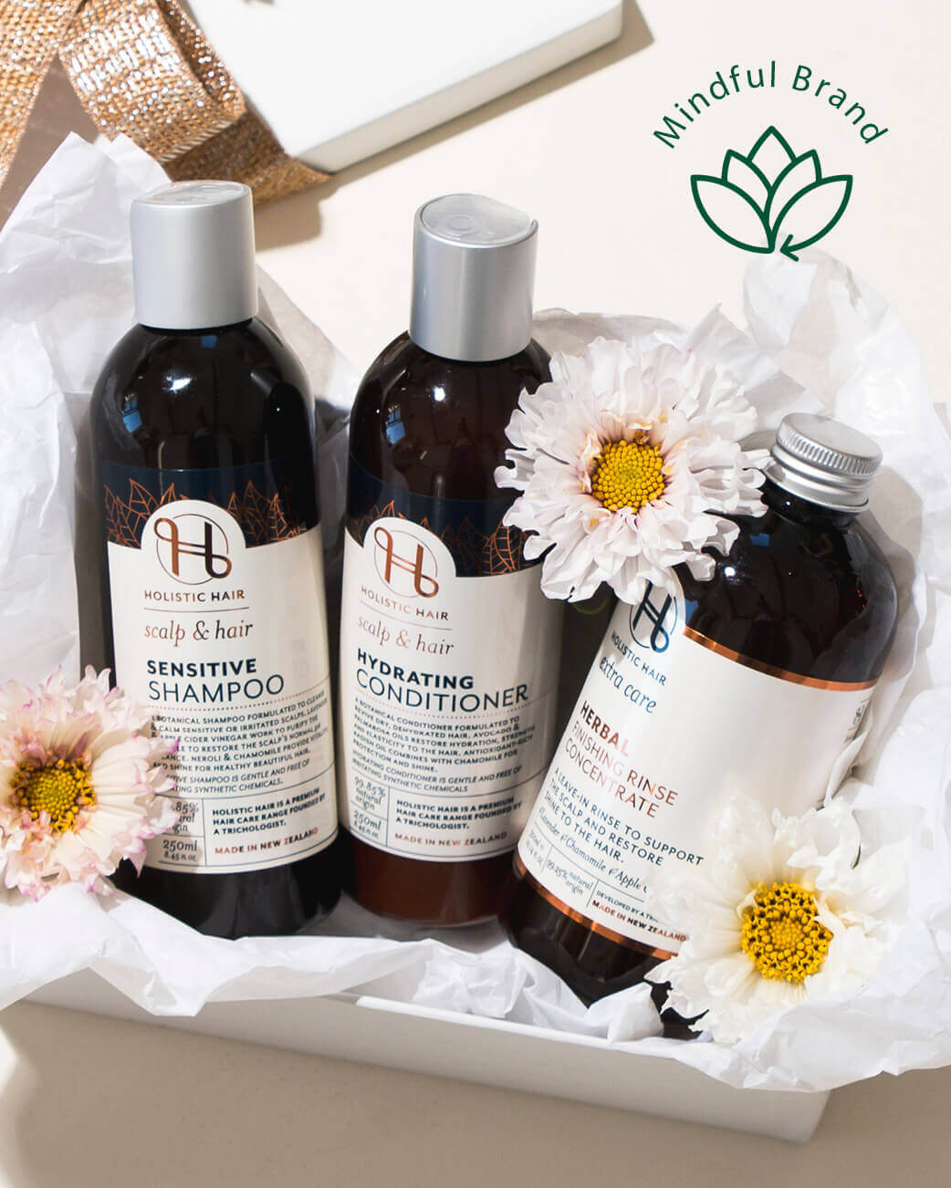 Three bottles of Holistic Hair care products with flowers on a white background, featuring the Mindful Brand logo.