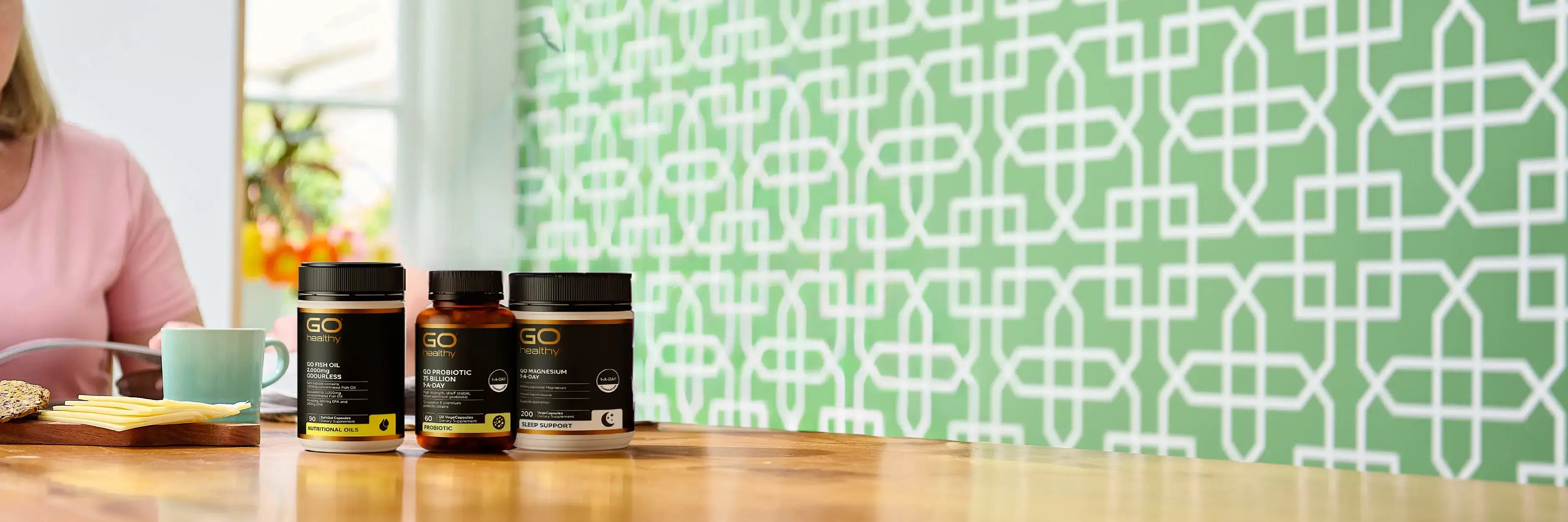 Three GO Healthy supplement bottles on a wooden surface against a green patterned wallpaper.