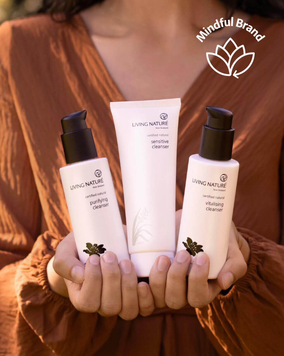 Three skincare products from the 'Living Nature' brand held by a person wearing an orange garment, with 'Mindful Brand' logo above.