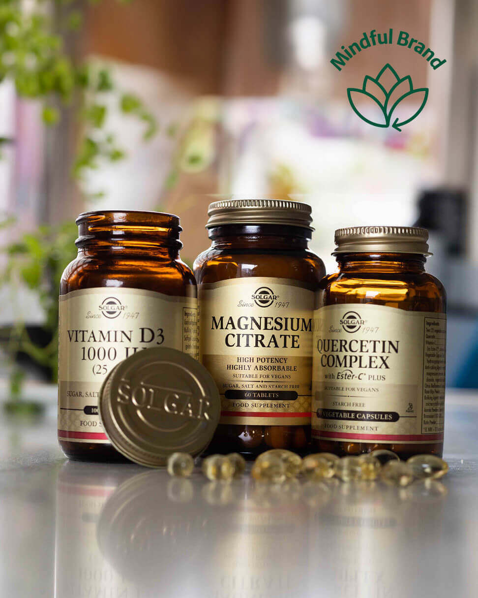 Three supplement bottles labelled Vitamin D3, Magnesium Citrate, and Quercetin Complex on a reflective surface with a blurred indoor background.