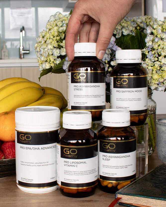 Supplement bottles labeled 'GO Healthy' on a kitchen counter with fruits and flowers in the background.