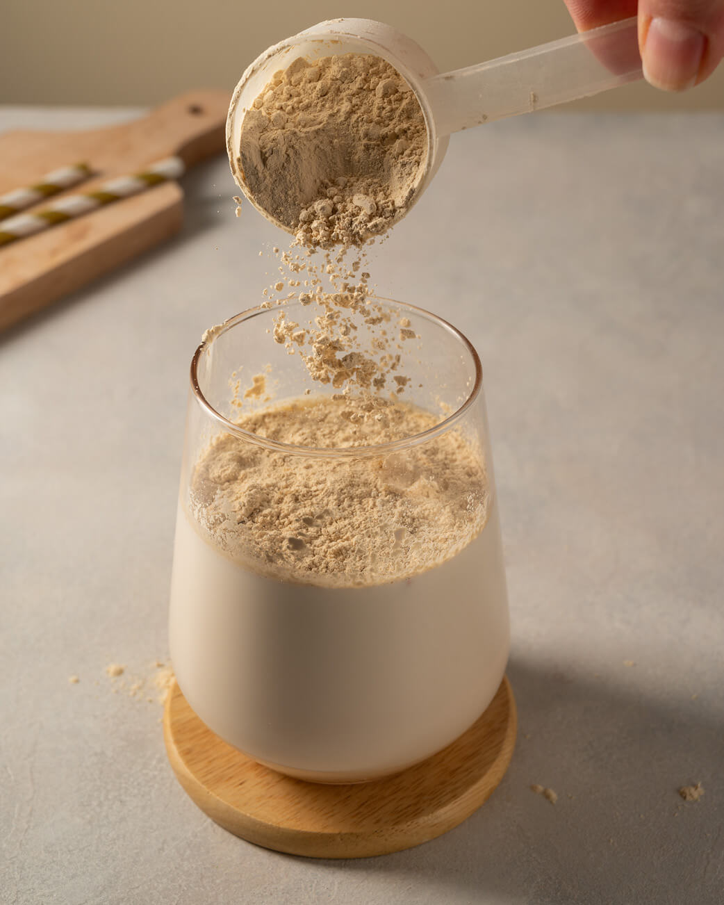 Powder being poured from a scoop into a glass on a neutral background