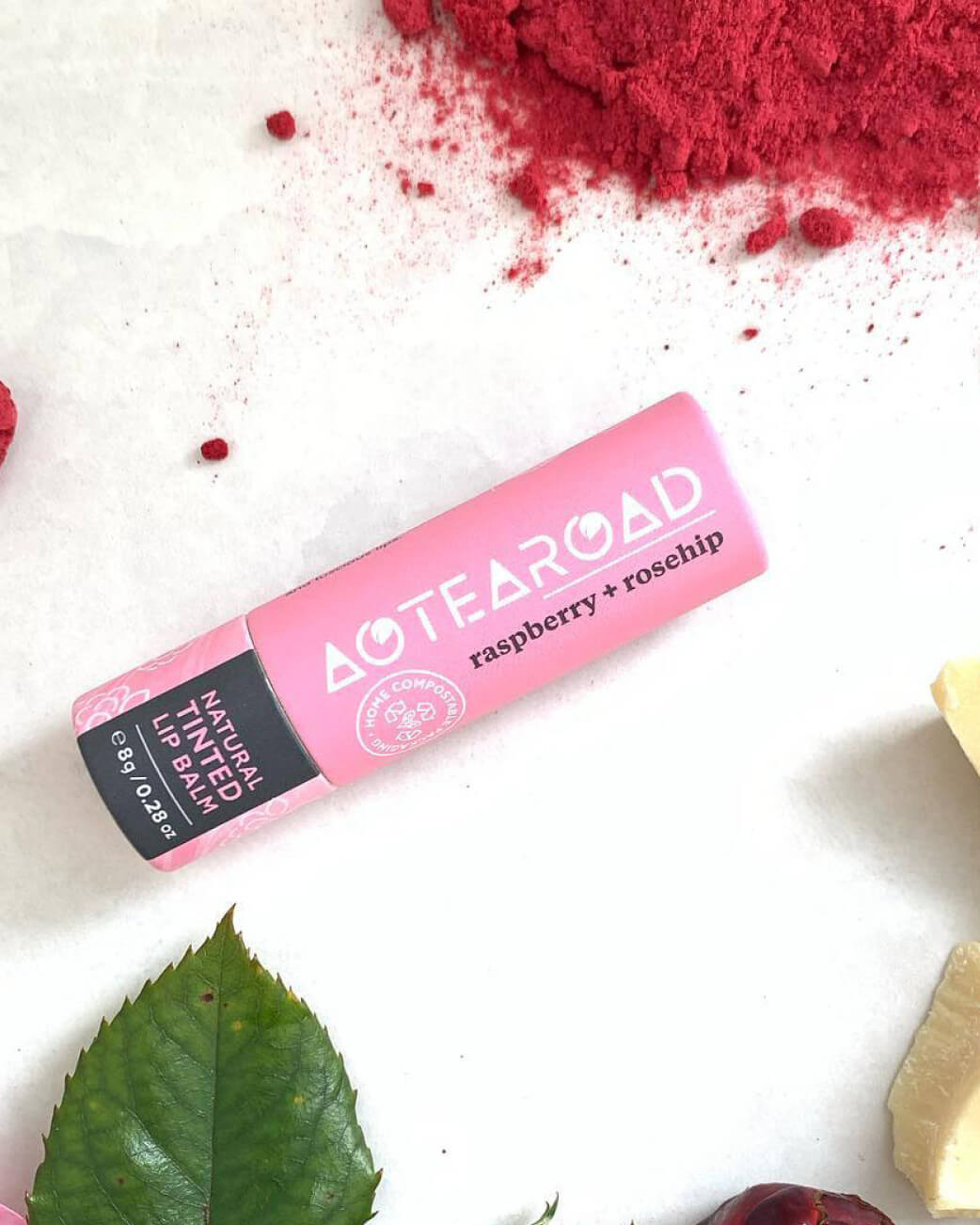 Pink lip balm from Aotearoad on a white background with red powder & green leaf