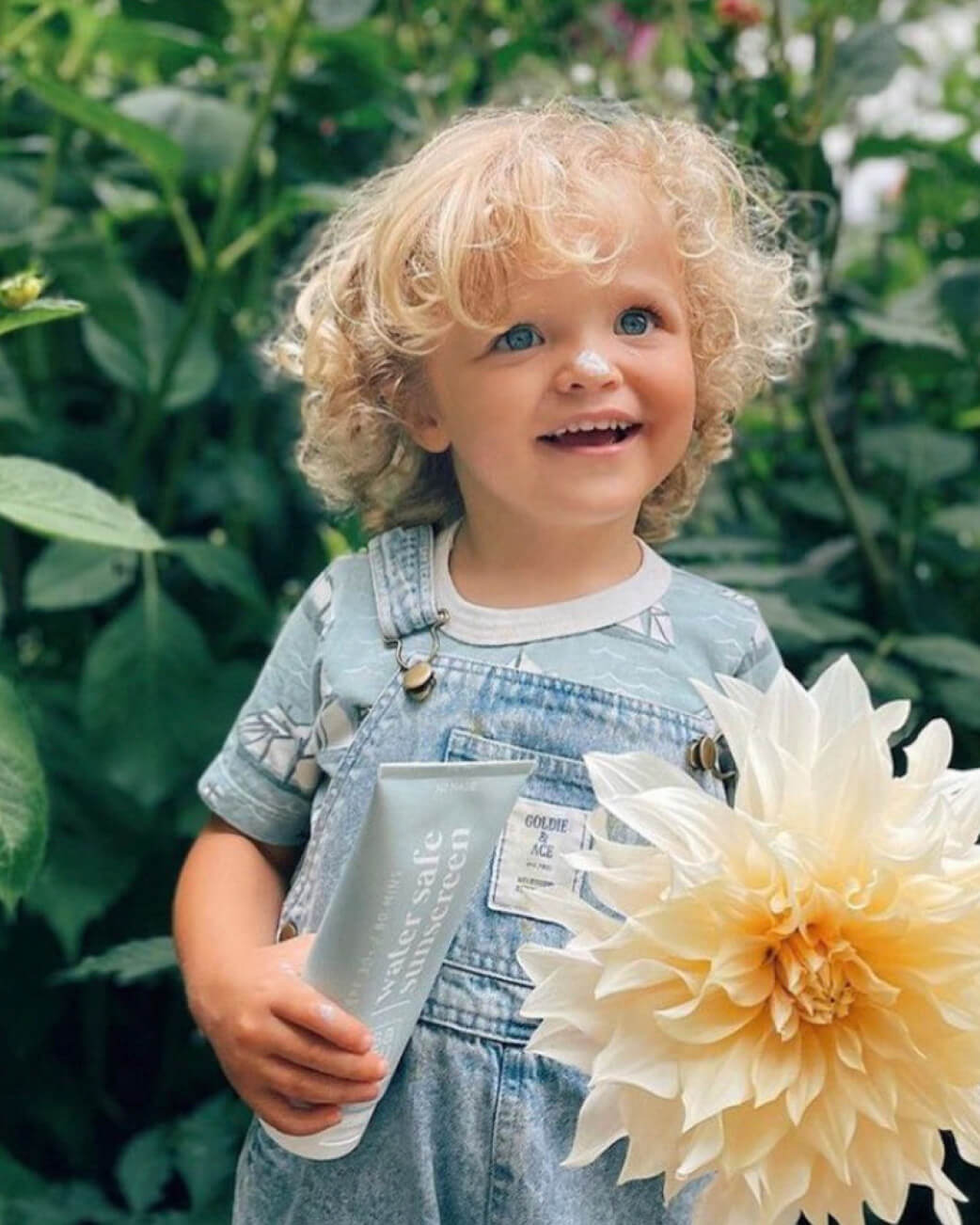Child holding a flower and a product container in a garden setting