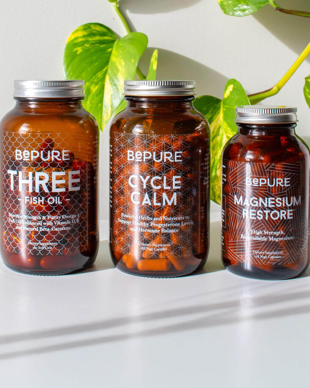 Three bottles of BePure supplements on a white surface with green leaves in the background