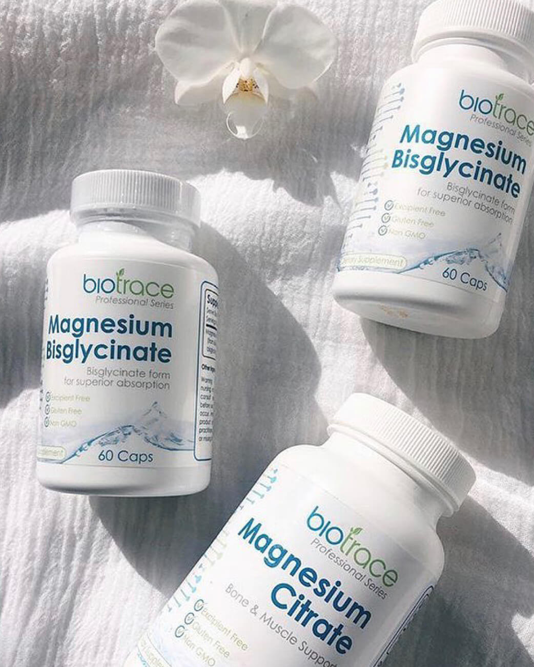 Three bottles of Biotrace magnesium supplements on a textured white surface with a white flower.