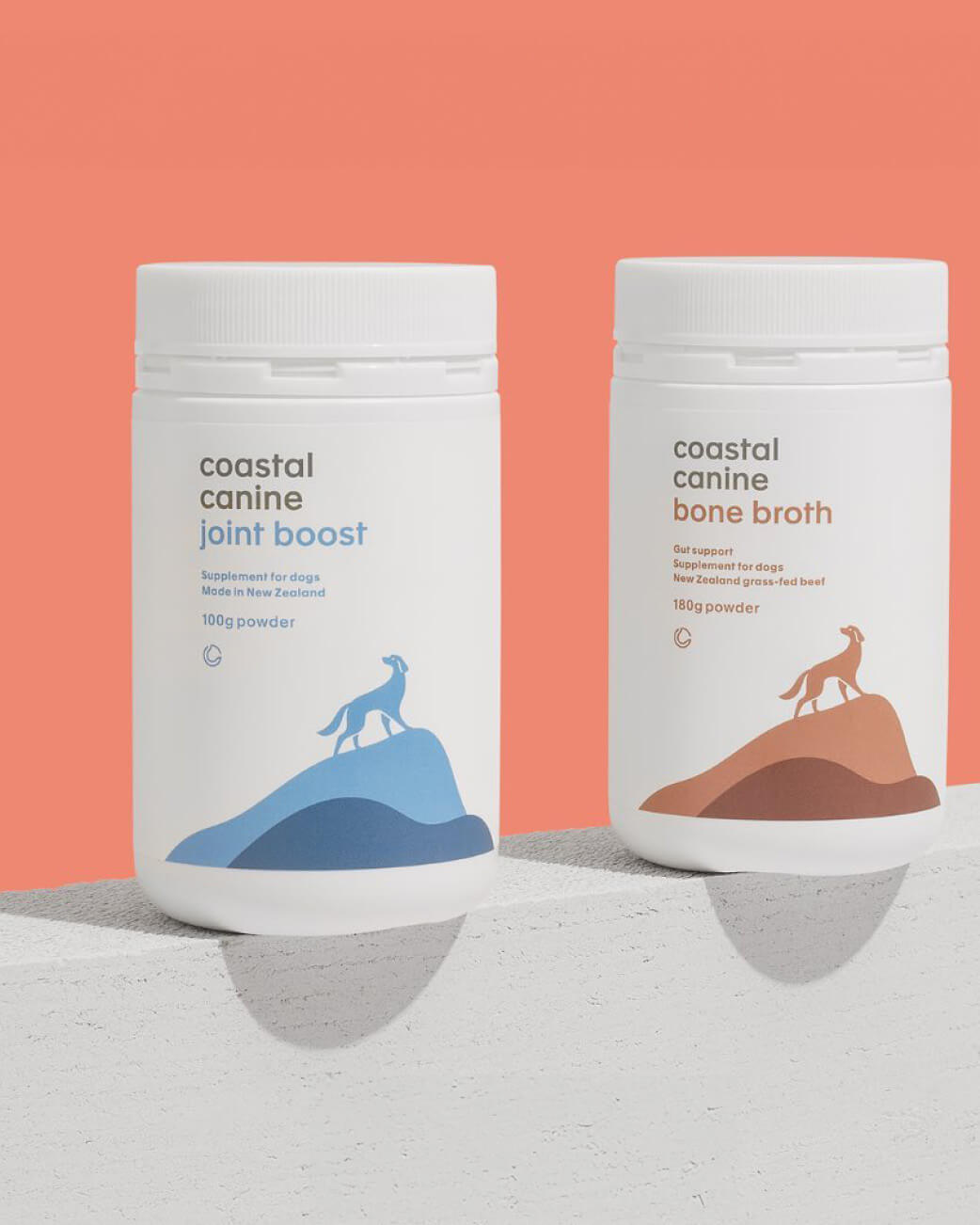 Two containers of coastal canine products on a gray surface with a peach background