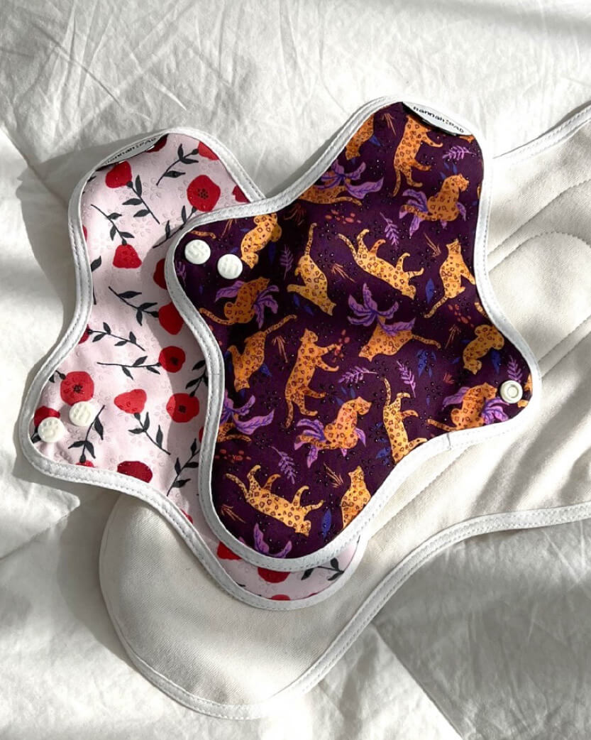Two reusable menstrual pads with floral and animal pattern on a white background.
