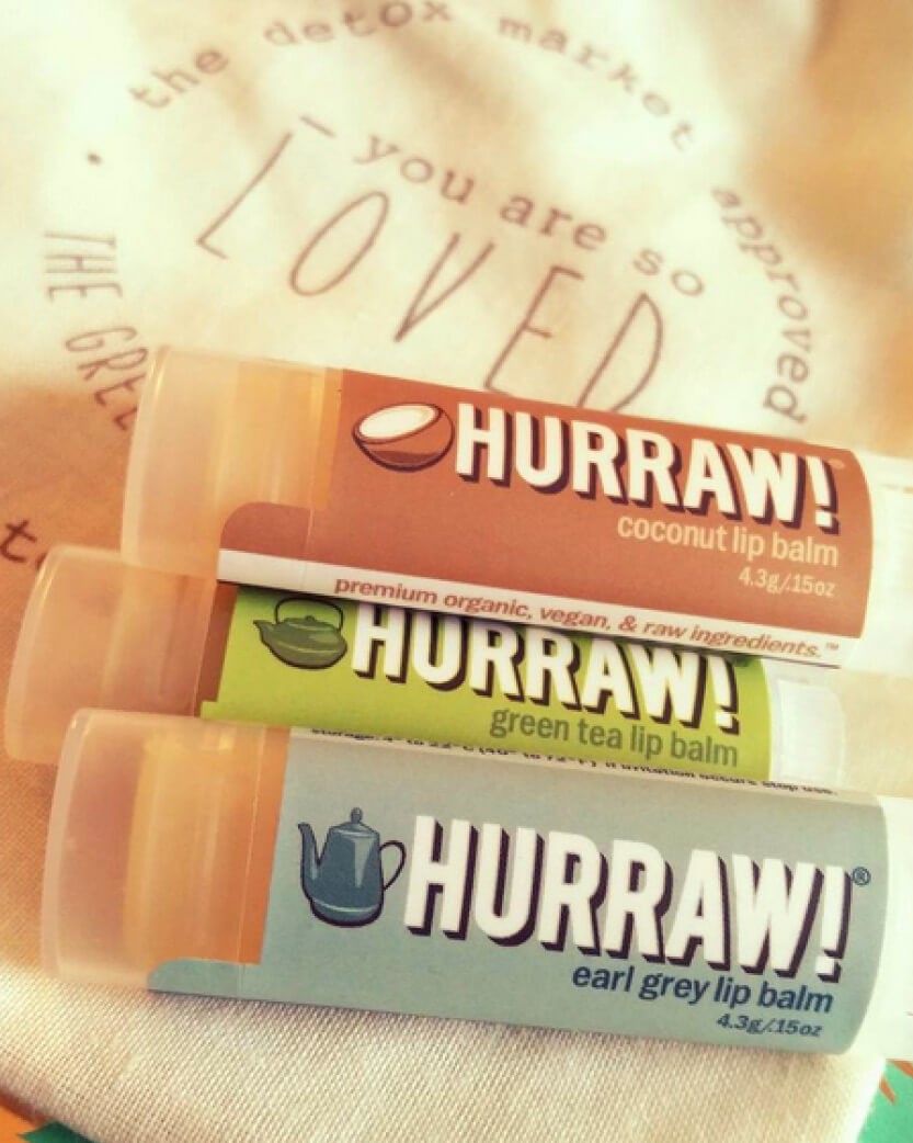 Three Hurraw! lip balms on a textured fabric background.