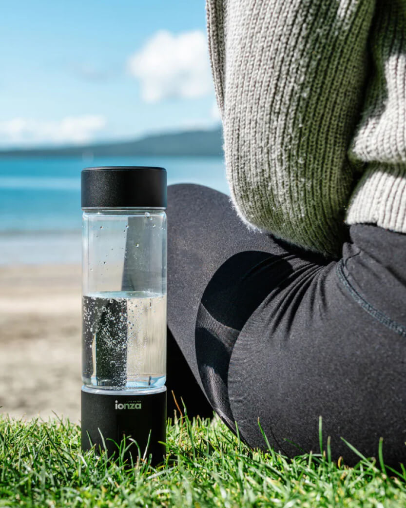 Person sitting on grass by a beach with an ionizer bottle.