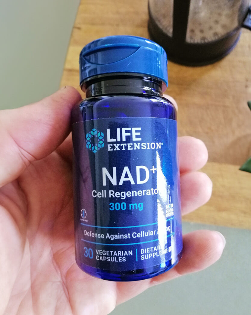 Life Extension NAD+ Cell Regenerator supplement bottle held in a hand on a wooden surface.