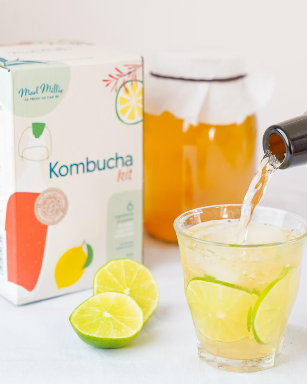 Kombucha kit with a glass of kombucha being poured, lime slices, and a box labelled 'Kombucha Kit'.