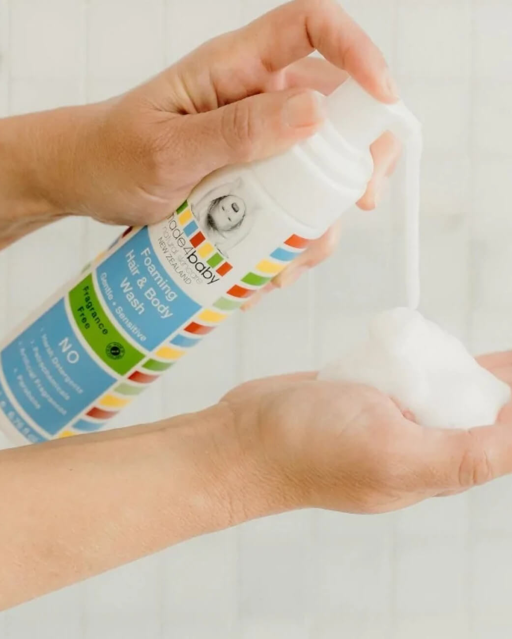 Hand holding a bottle of baby wash with a colourful label against a plain background.