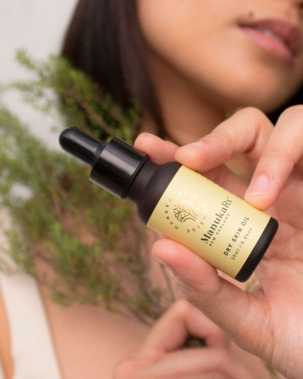 Person holding a bottle of Manukarx hair oil with a blurred background.