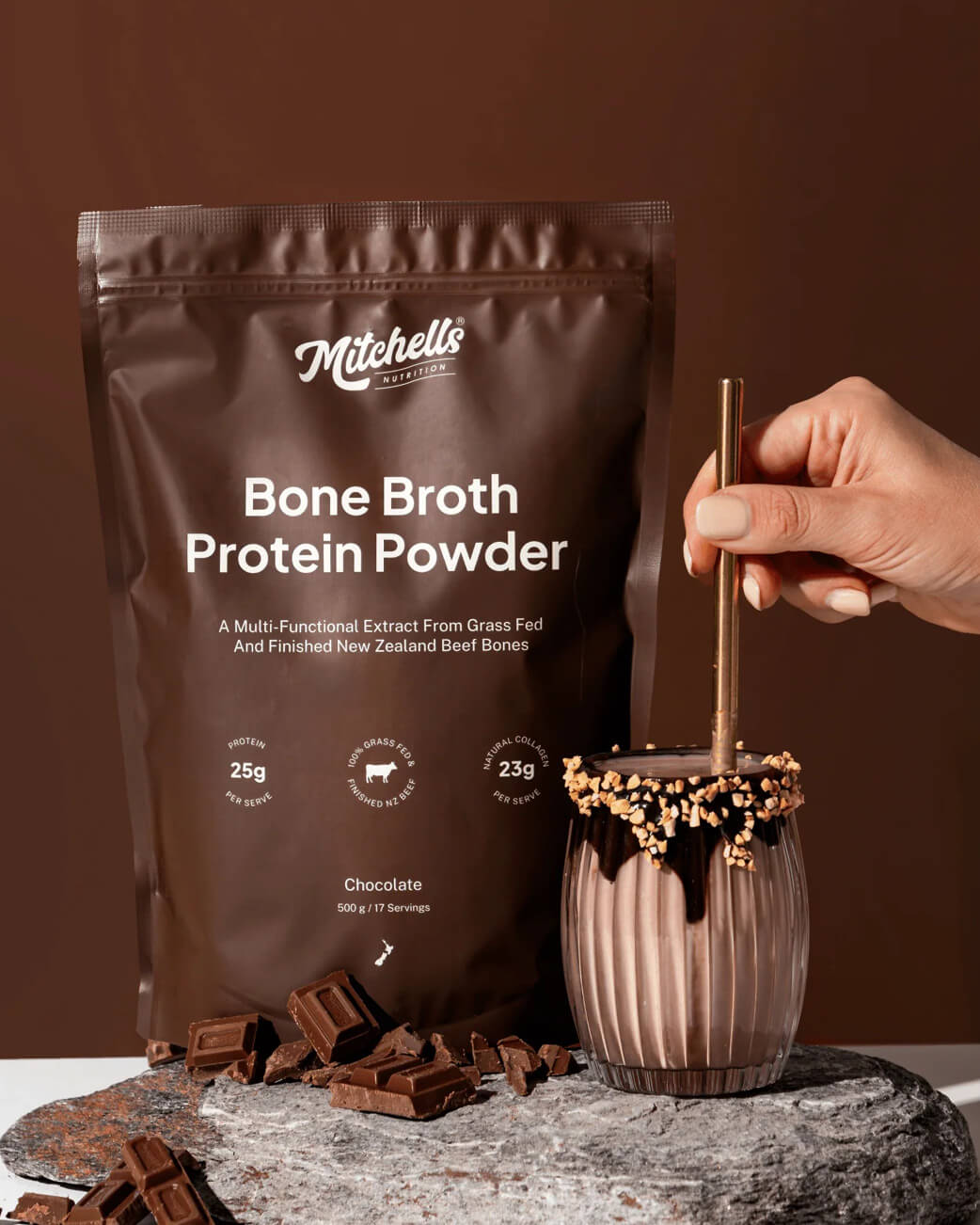 Mitchell's Bone Broth Protein Powder with a chocolate protein shake and chocolate pieces on a brown background.