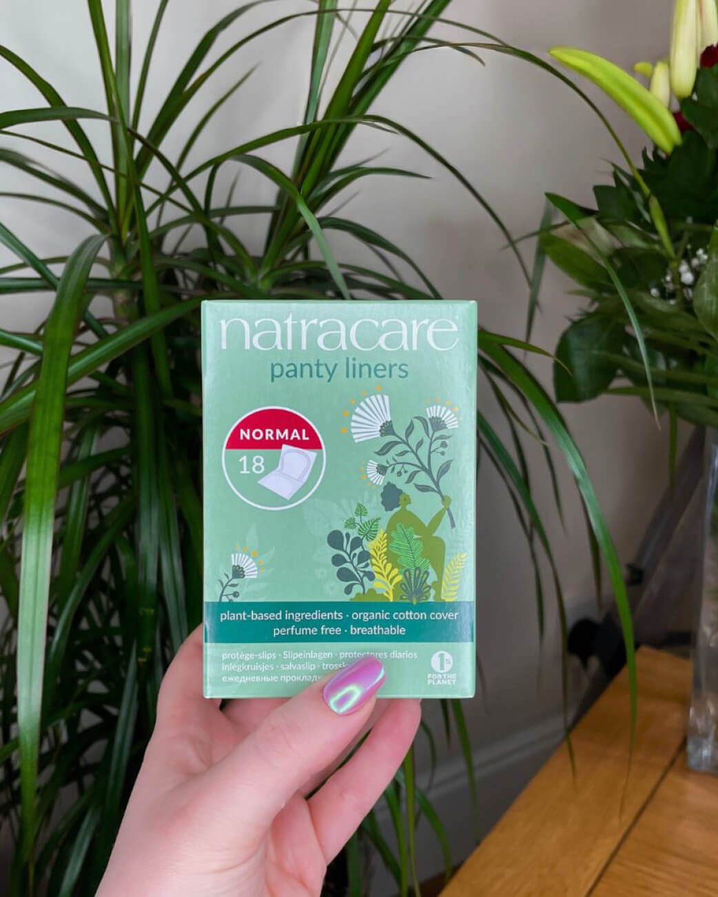 Hand holding a box of Natracare panty liners in front of a plant.