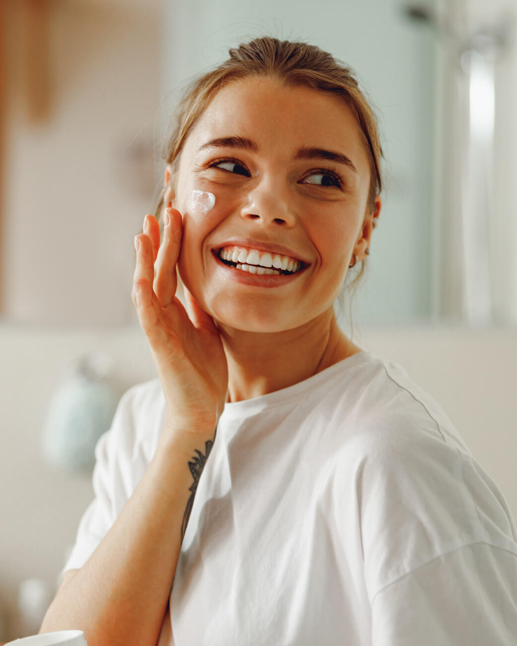 Woman applying cream to her face in a bright room.