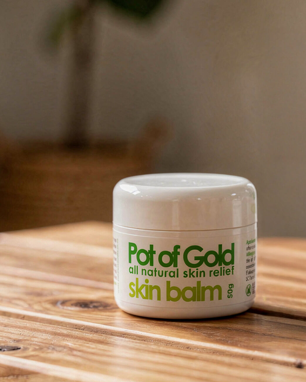 Jar of Pot of Gold skin balm on a wooden surface with a blurred background.