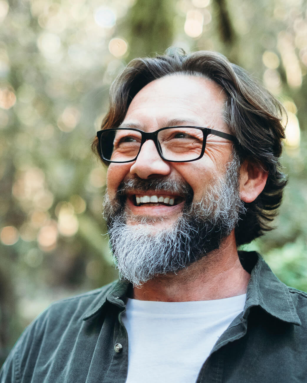 Man with glasses and a beard smiling outdoors.
