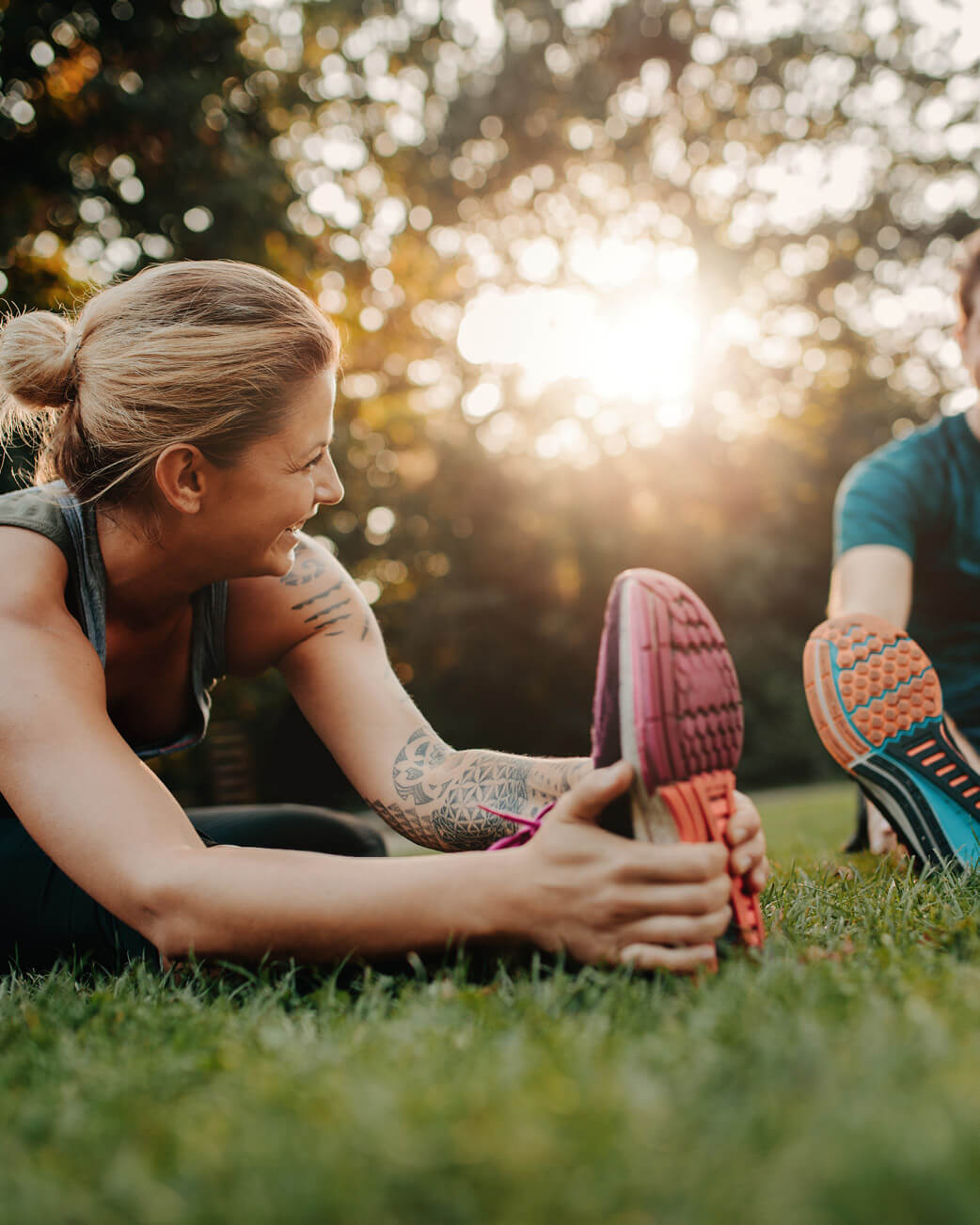Woman stretching outdoors with a blurred background of trees and sunlight.