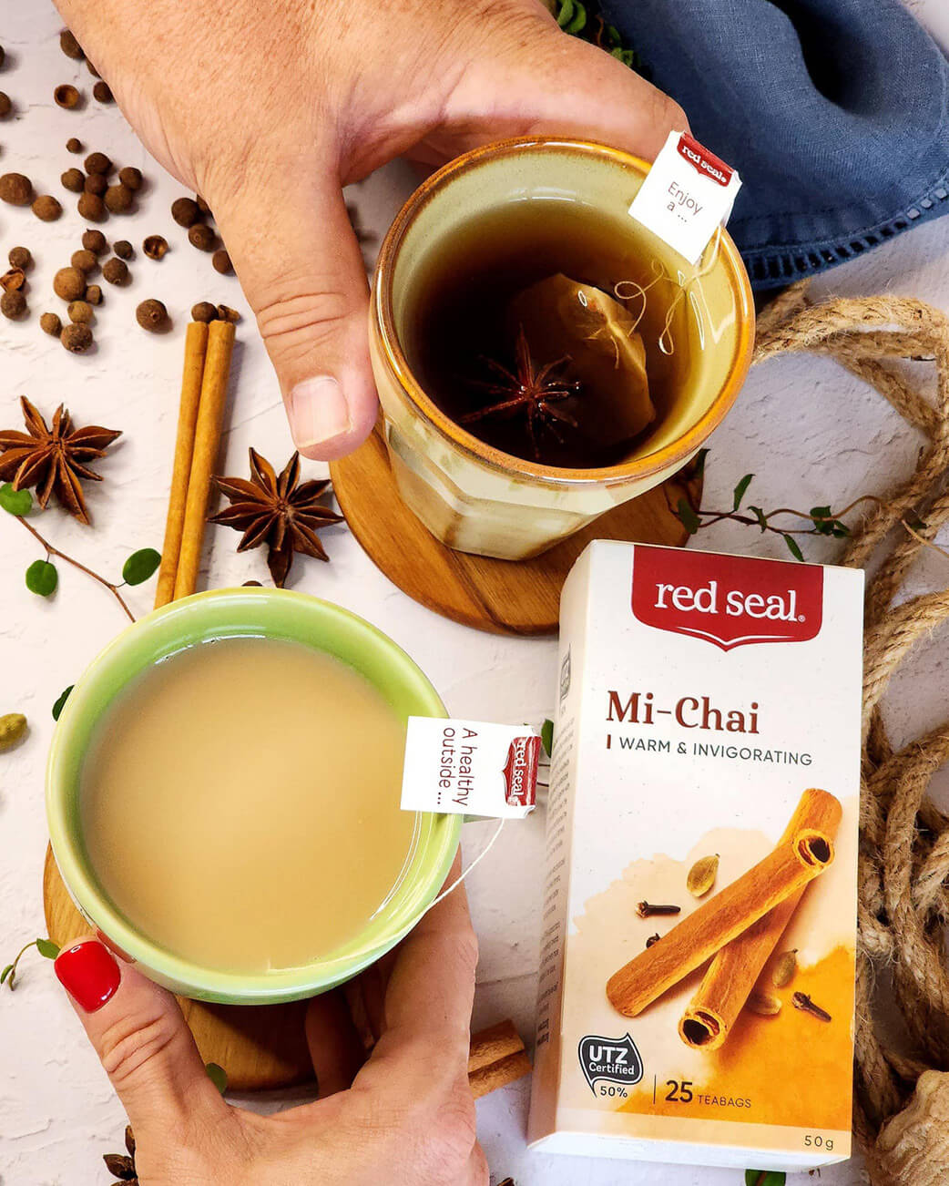 Two hands holding cups of tea with a Red Seal Mi-Chai box on a decorative background.