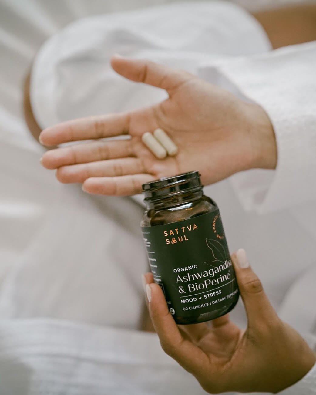 Person holding a bottle of Sattva Soul supplements with pills in their hand.