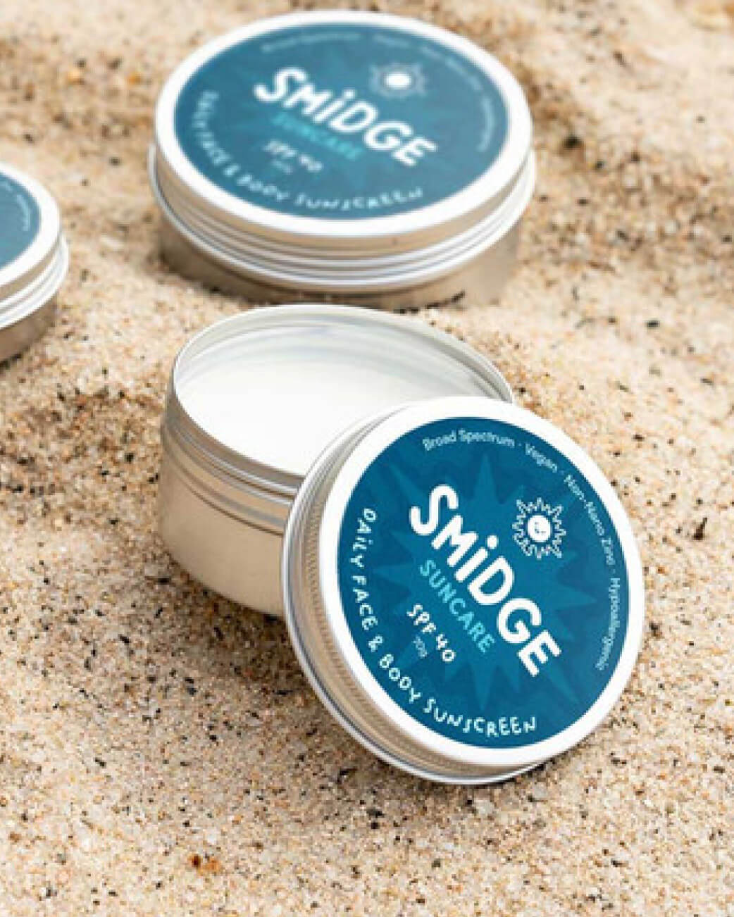 Smidge sunscreen tins on sand.