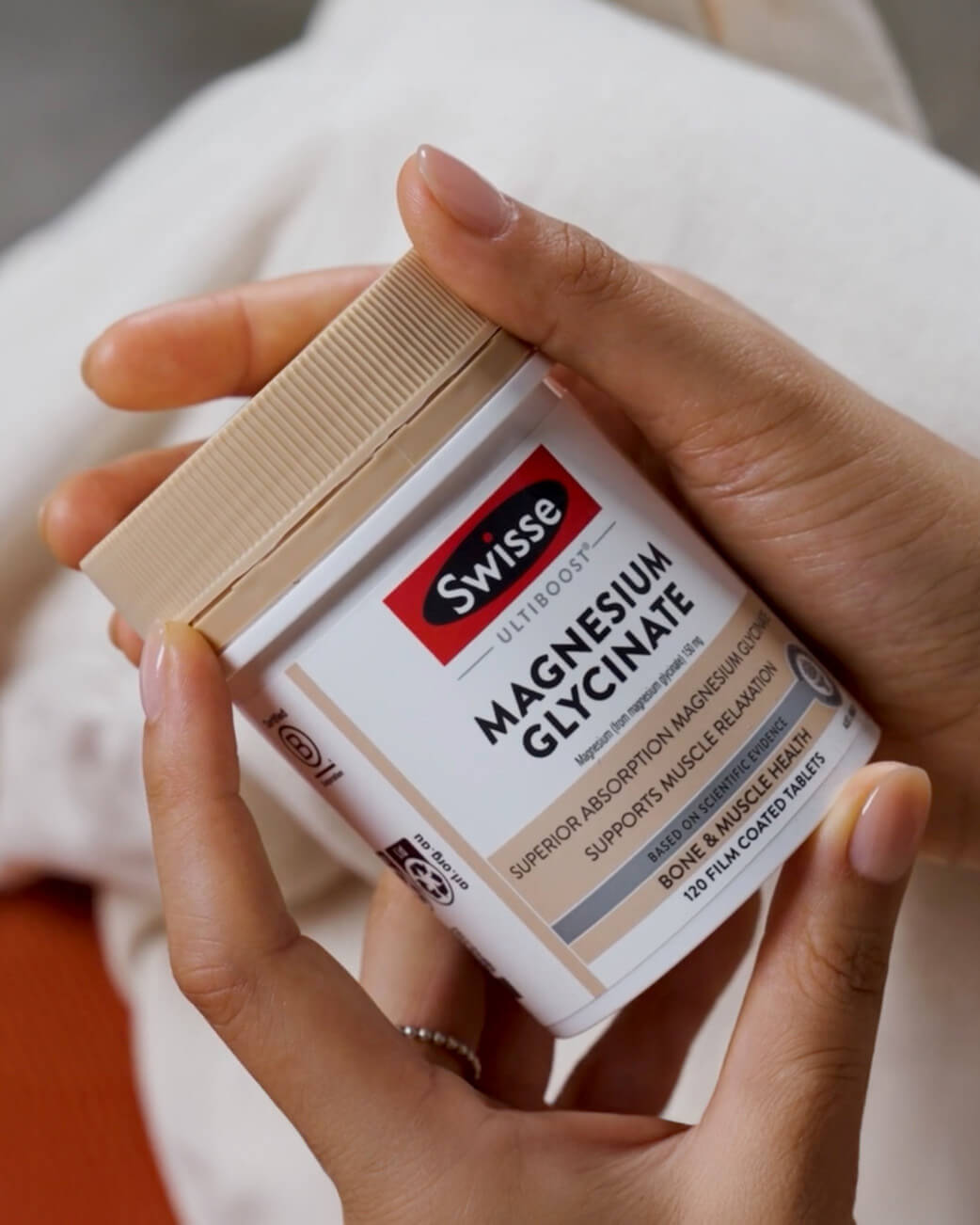 Person holding a Swisse supplement container labeled 'Magnesium Glycinate'.