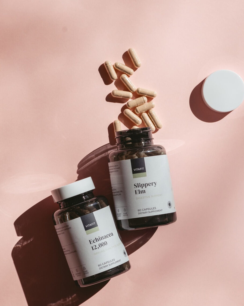 Two bottles of supplements with scattered capsules on a pink background.