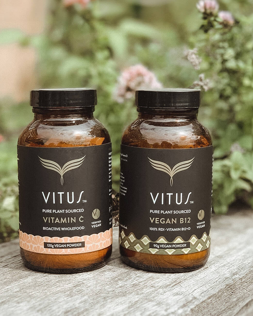 Two bottles of Vitus vegan powder on a wooden surface with a natural background.