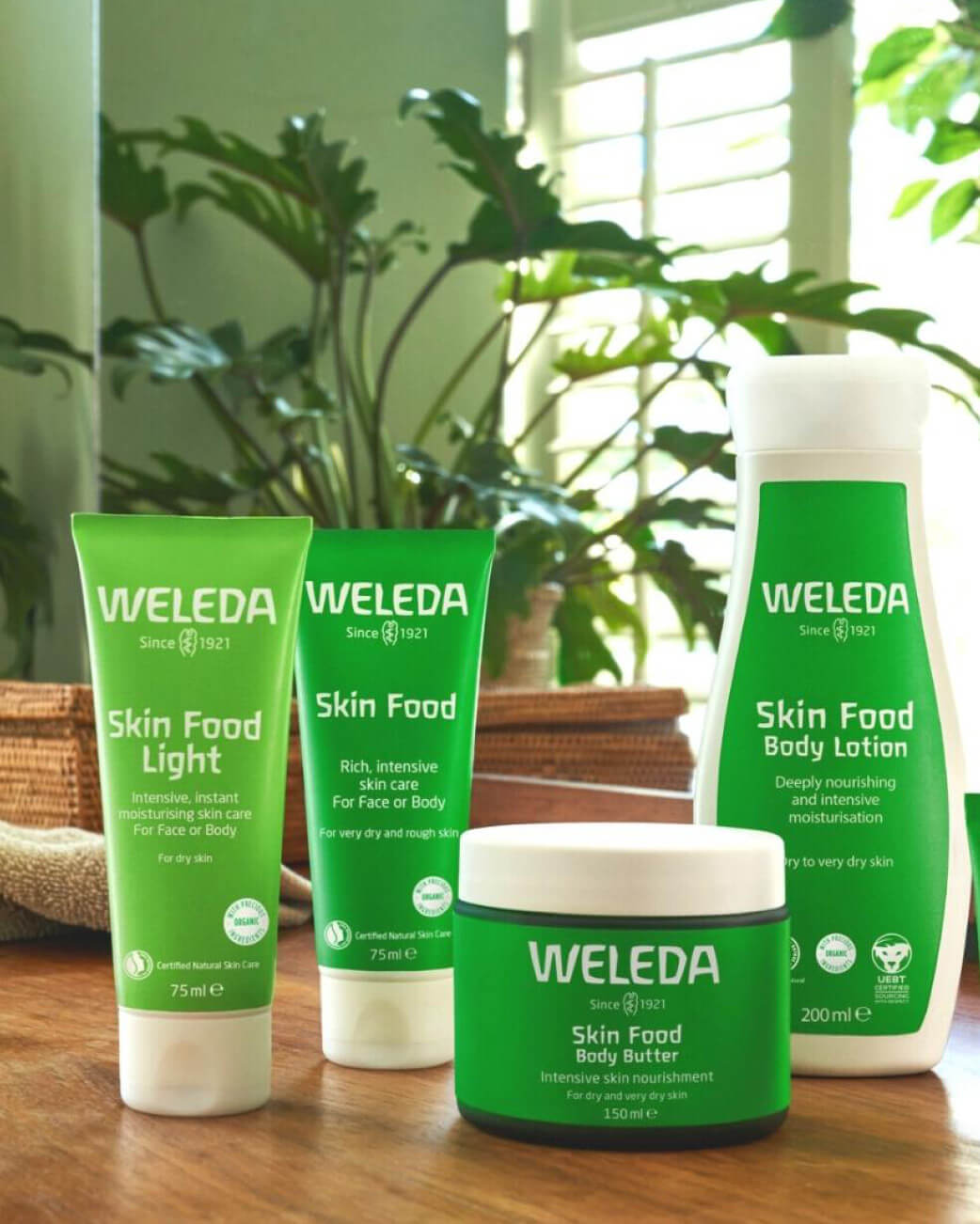Weleda Skin Food products on a wooden surface with plants in the background.