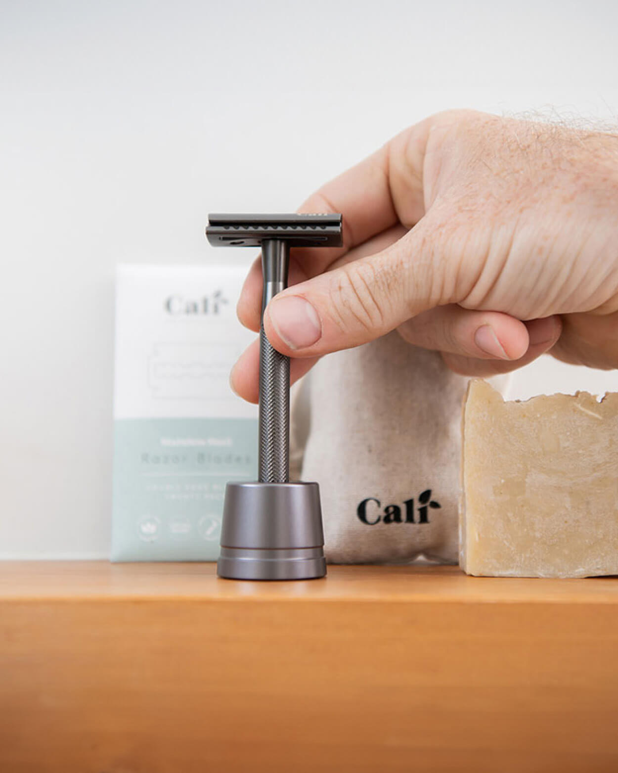Hand placing a grey stainless steel razor in a stand on a wooden surface.
