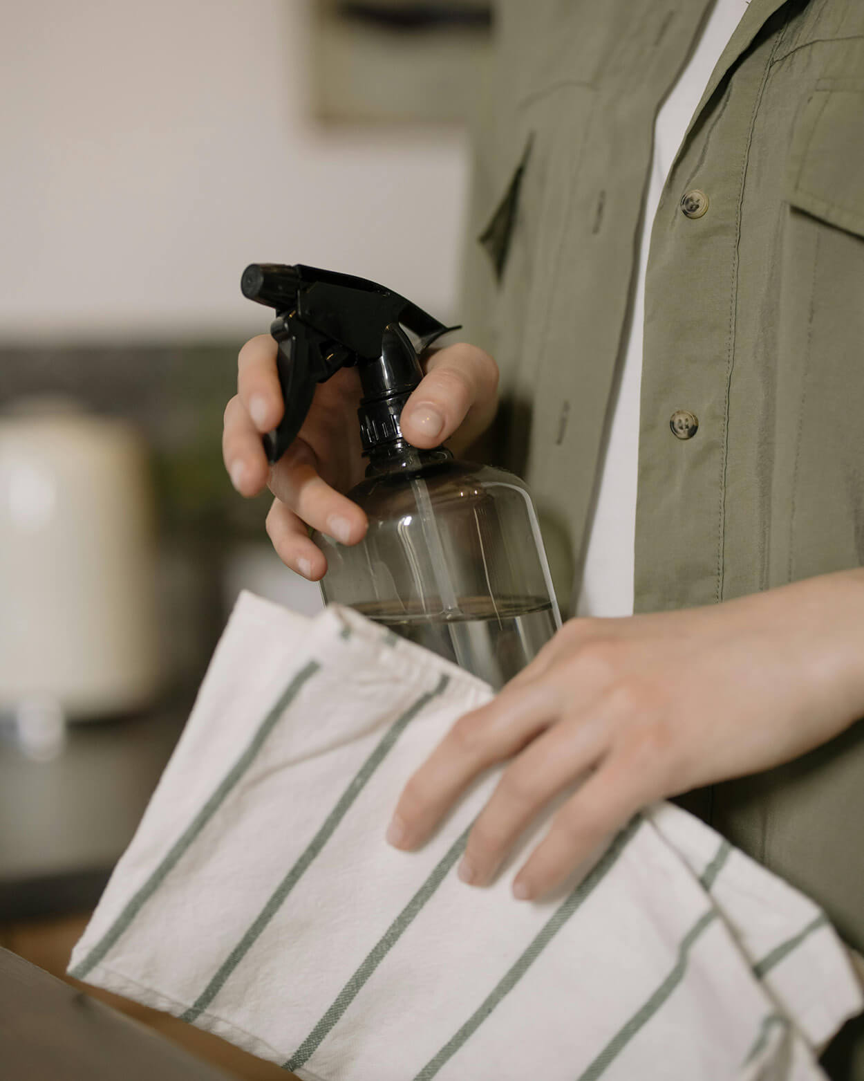 Person holding a spray bottle and a striped towel in a kitchen setting.