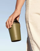 Person holding a green reusable coffee cup against a clear blue sky.