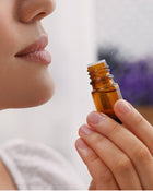 Person holding a small brown essential oil bottle with a blurred background.