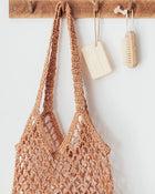 Brown crochet bag hanging on a wooden hook with a white background