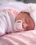 Newborn baby sleeping with a pacifier in a pink & white polka dot blanket.