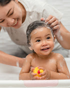Woman washing a child's hair with a yellow rubber duck in the bathtub.