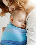 Woman holding a sleeping baby wrapped in a blue swaddle.