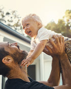 Man holding a baby outdoors with trees in the background.