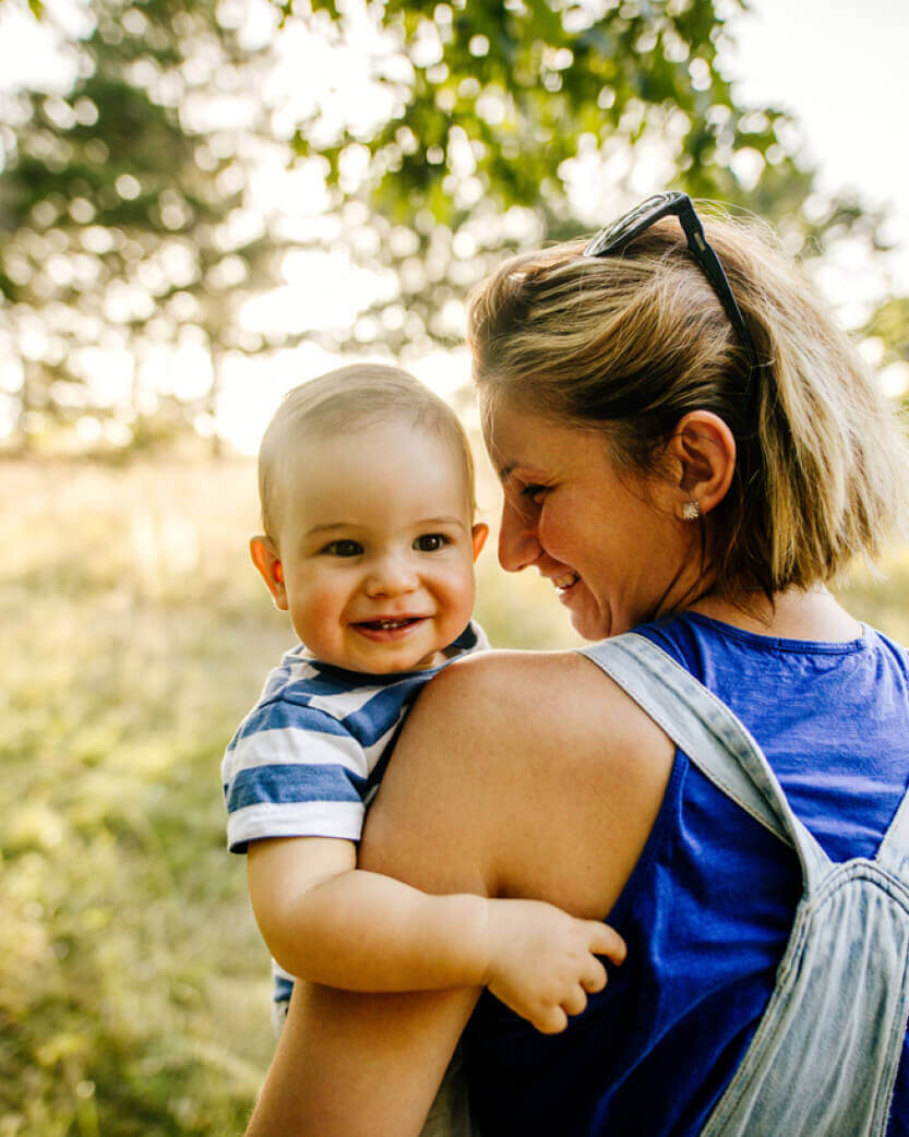 Woman holding a baby outdoors with trees in the background.