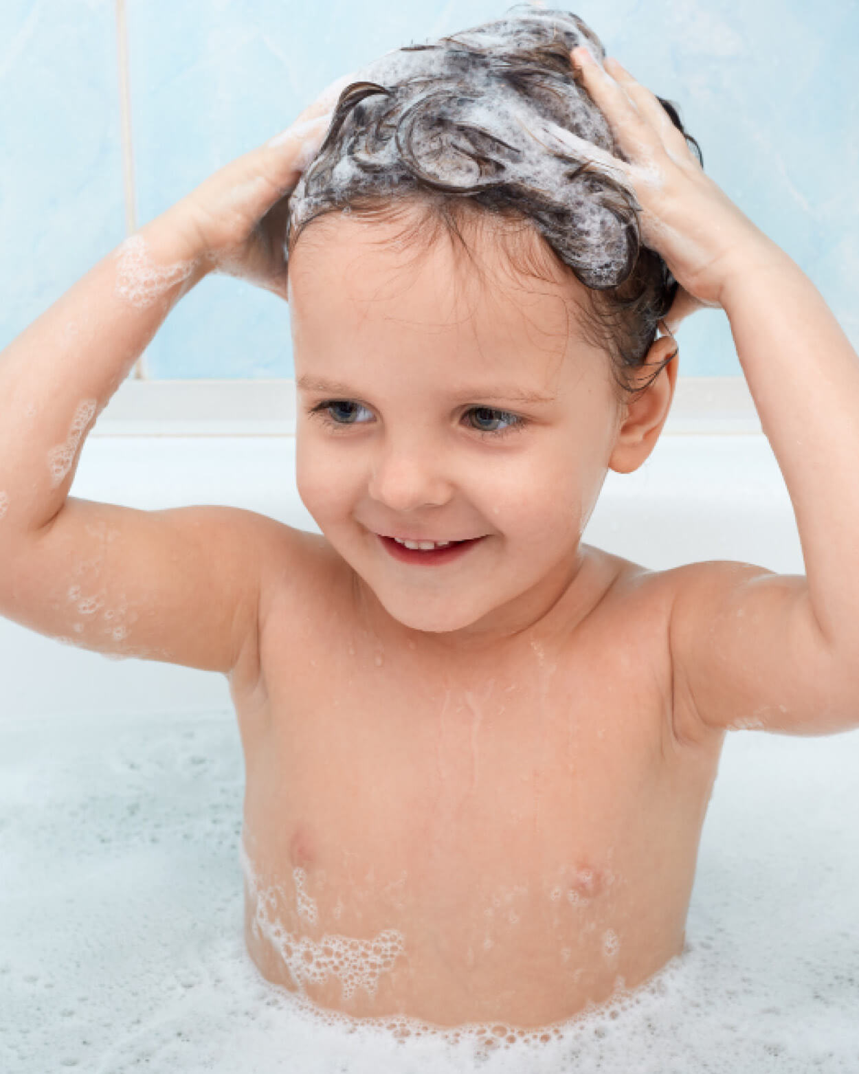 Child with soapy hair in a bathtub, smiling.