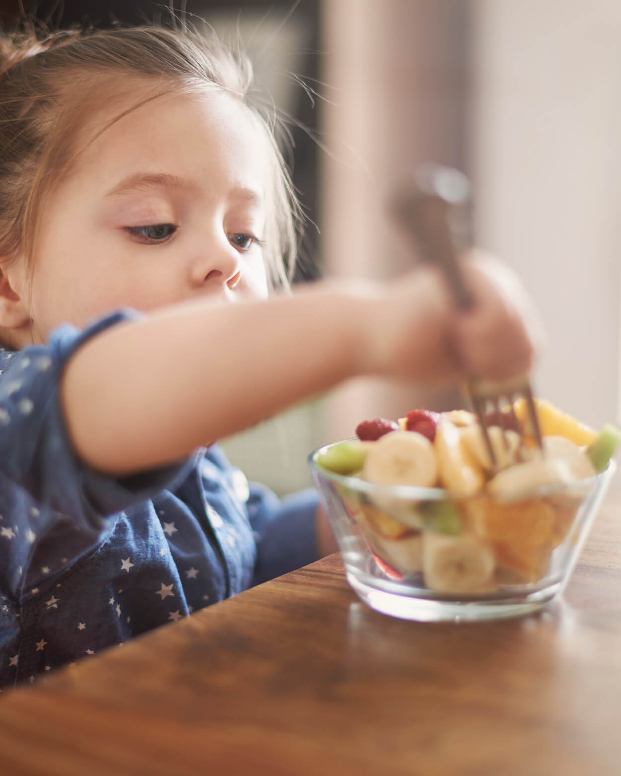Child reaching for a fruit salad in a bowl at a wooden table.