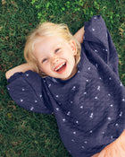 Child wearing a navy blue quilted jacket with white patterns, lying on grass and smiling.