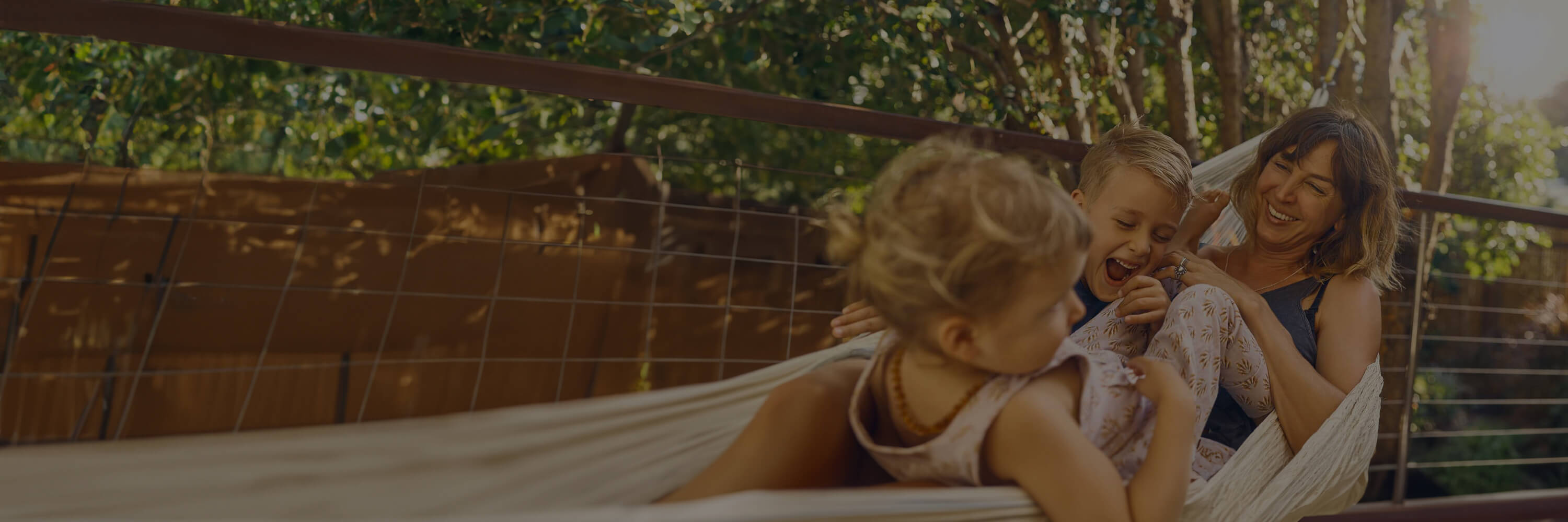 Woman and two kids smiling in a hammock outside.