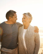 Man and woman standing close together on a beach, smiling at each other.