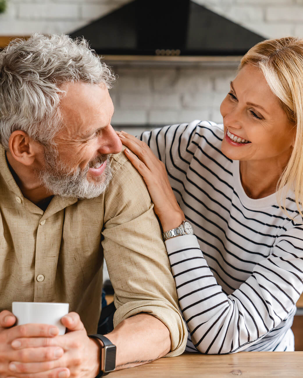 Man and woman sitting together in a kitchen, smiling and enjoying each other's company.