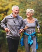 Two elderly people jogging outdoors with a blurred green background.