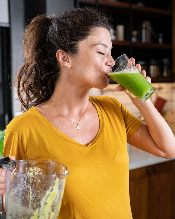 Woman drinking green juice from a glass in a kitchen.